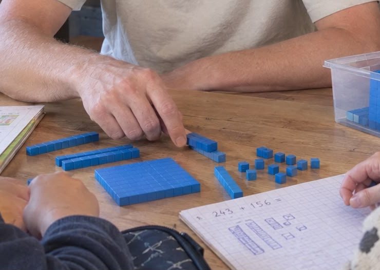 Bart wijst rekenblokjes aan terwijl een leerling de som 243 + 156 uitwerkt in een ruitjesschrift